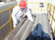 Trabajador usa traje de protección y manipula una placa de fibrocemento con amianto sobre una plataforma elevadora.