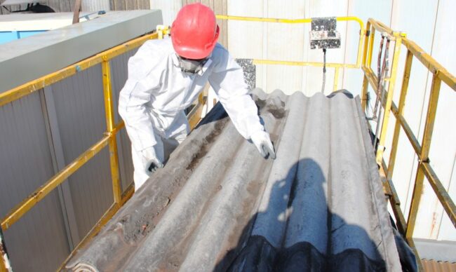 Retirada-Amianta-Epis-Uralita-Fibrocemento-pk Trabajador usa traje de protección y manipula una placa de fibrocemento con amianto sobre una plataforma elevadora.