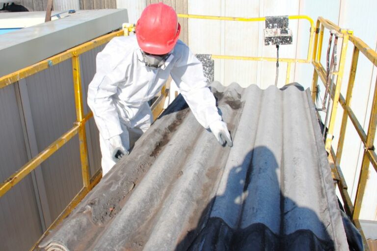 Trabajador usa traje de protección y manipula una placa de fibrocemento con amianto sobre una plataforma elevadora.