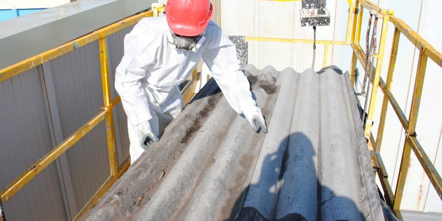 Trabajador usa traje de protección y manipula una placa de fibrocemento con amianto sobre una plataforma elevadora.